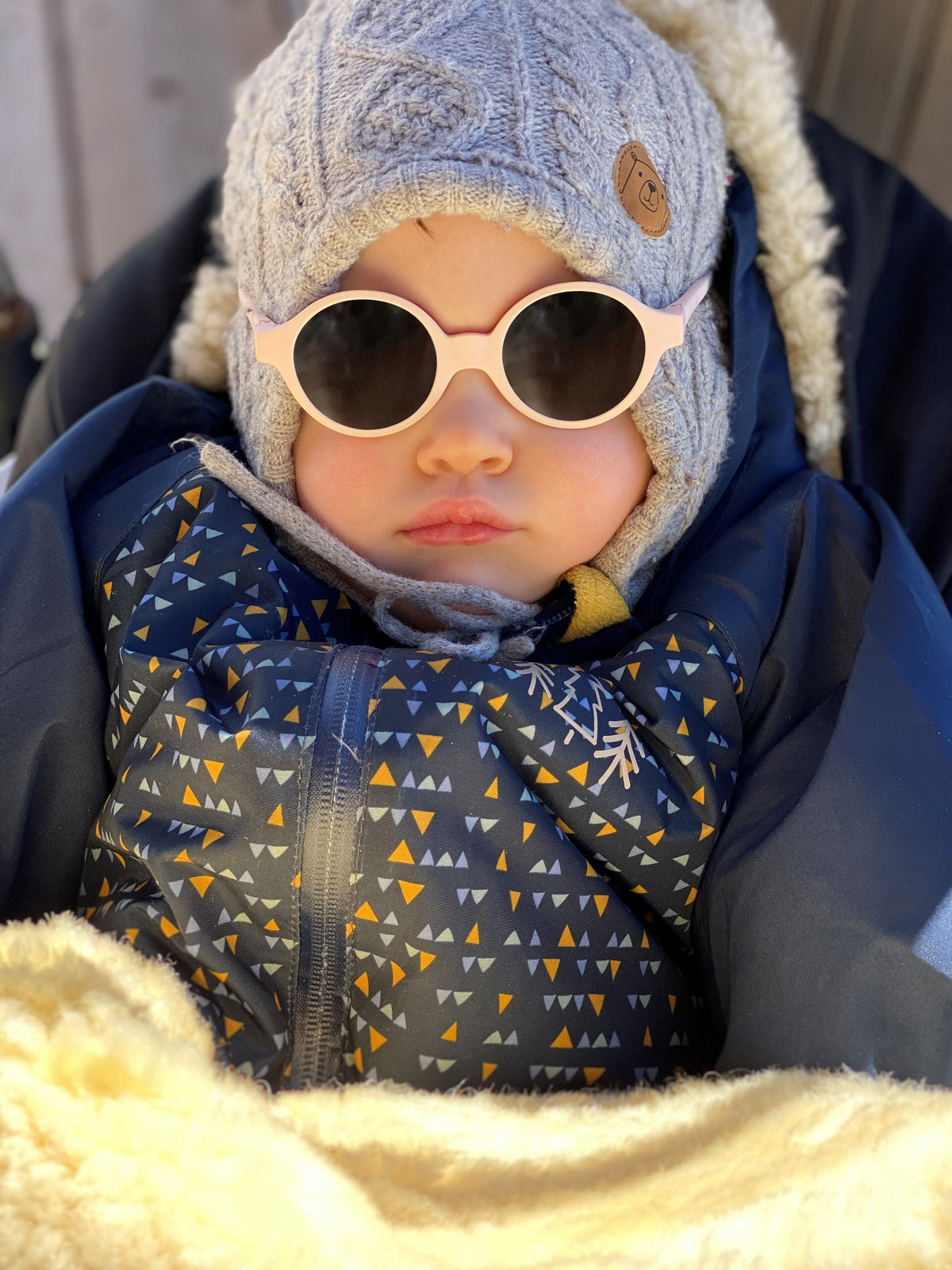 Infant wearing pink Joy sunglasses while seated in a stroller