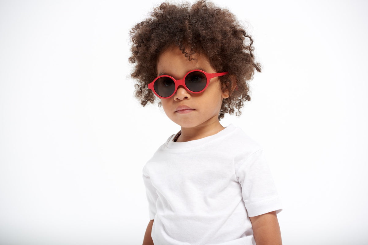 Front view of Joy Infant Sunglasses in Poppy Red showcasing round red frames worn by a child against a white background