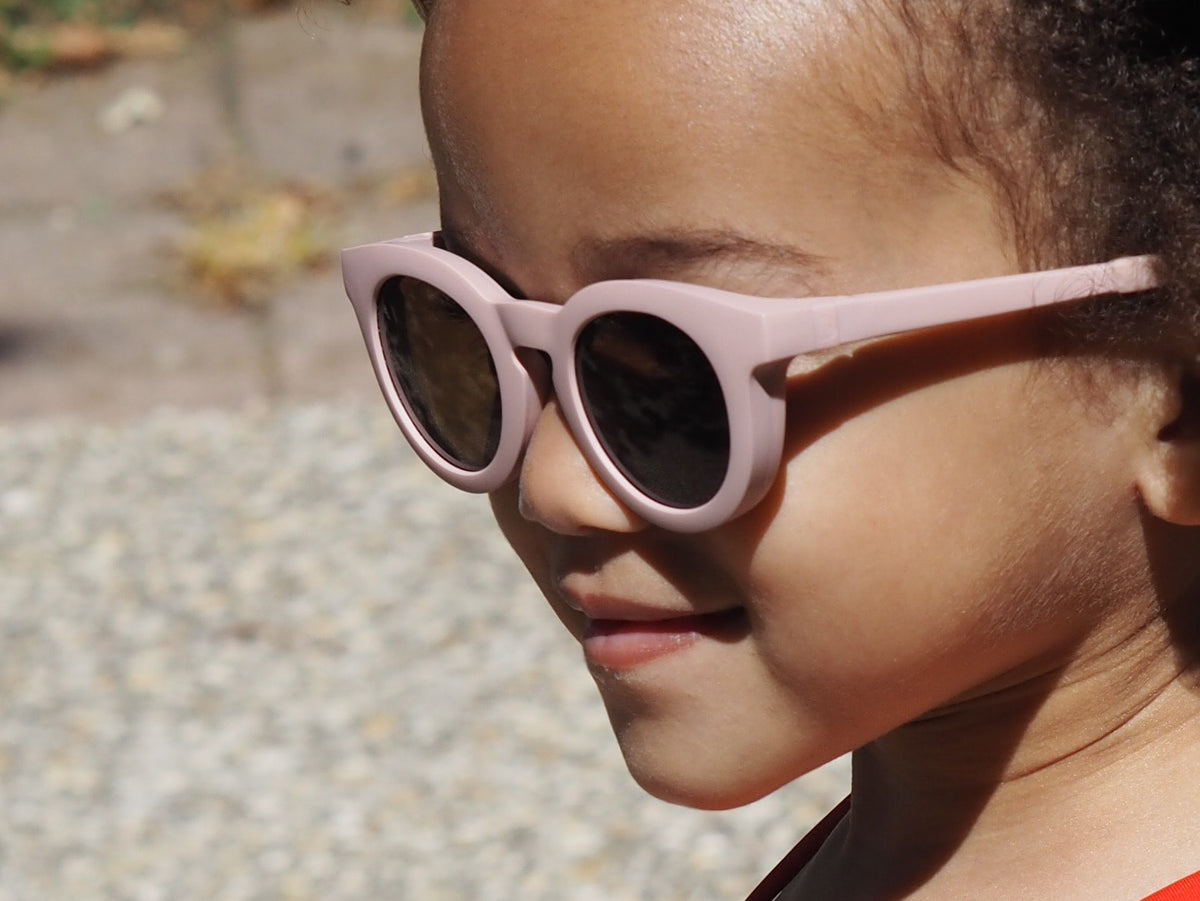 Close-up side view of Happy Infant Sunglasses in Dusty Pink showcasing dark lenses on a child outdoors