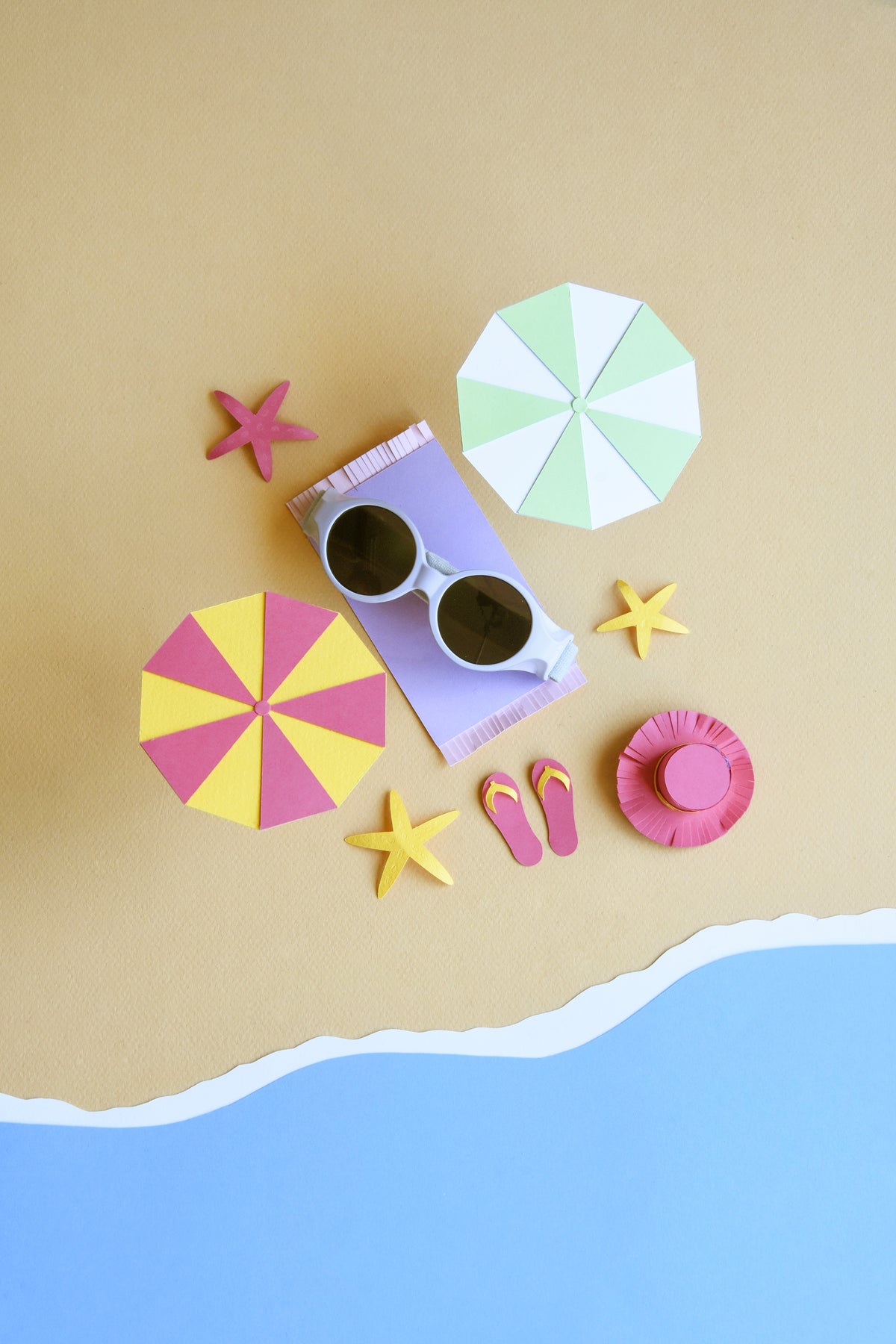 Top view of Glee Infant Sunglasses in Lilac showcasing dark lenses and elasticated headband with a colorful beach-themed background