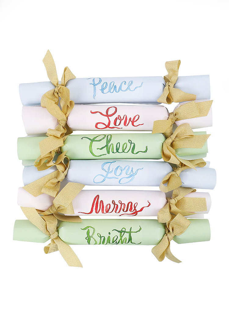 Stacked set of 6 holiday crackers with pastel papers, gold ribbon bows, and calligraphy words Peace, Love, Cheer, Joy, Merry, Bright