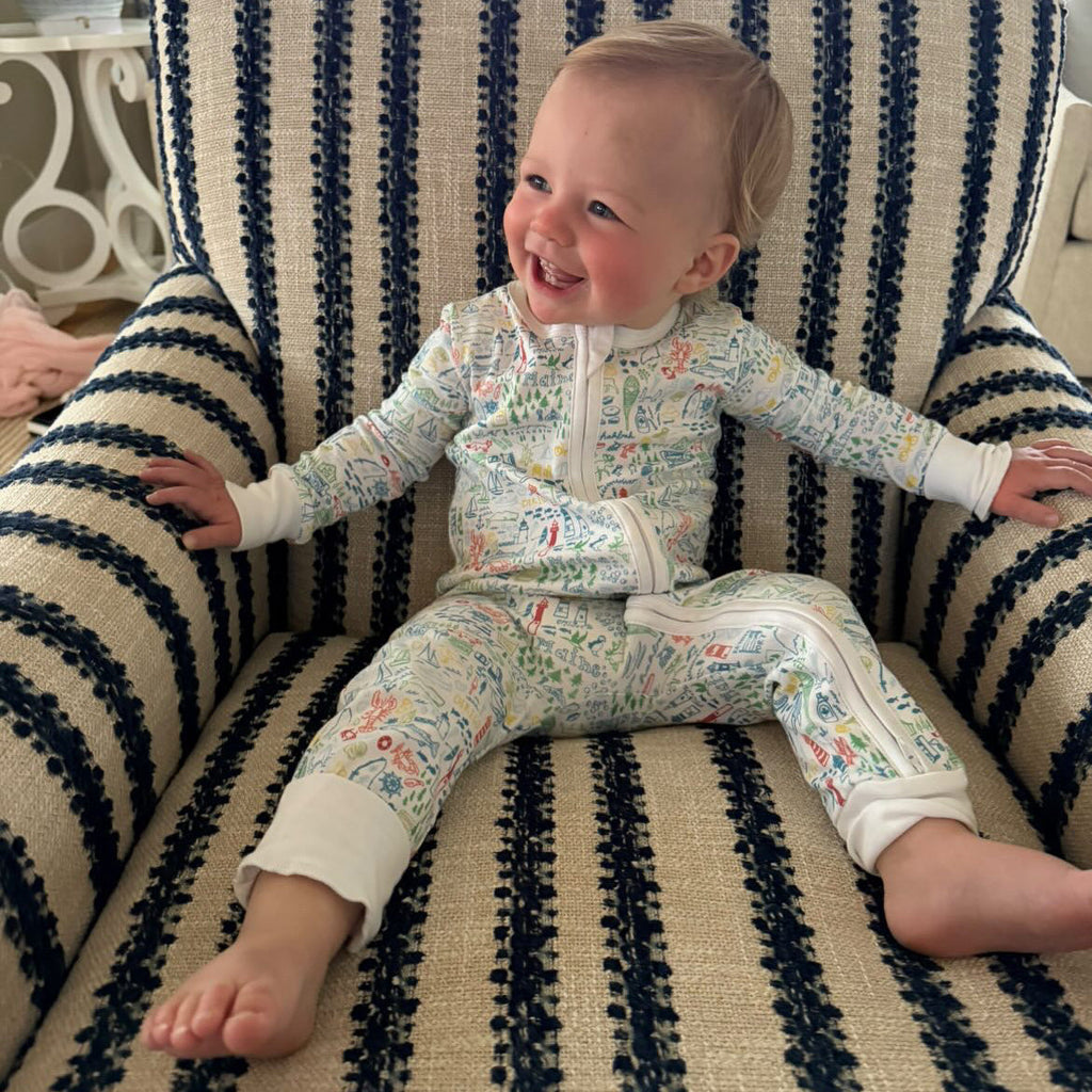 Front view of Maine Zip Baby Onesie showcasing hand-drawn Maine landmark print in a footless fit on a baby seated in a striped chair