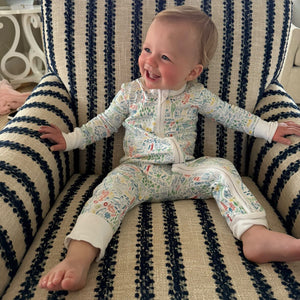 Front view of Maine Zip Baby Onesie showcasing hand-drawn Maine landmark print in a footless fit on a baby seated in a striped chair
