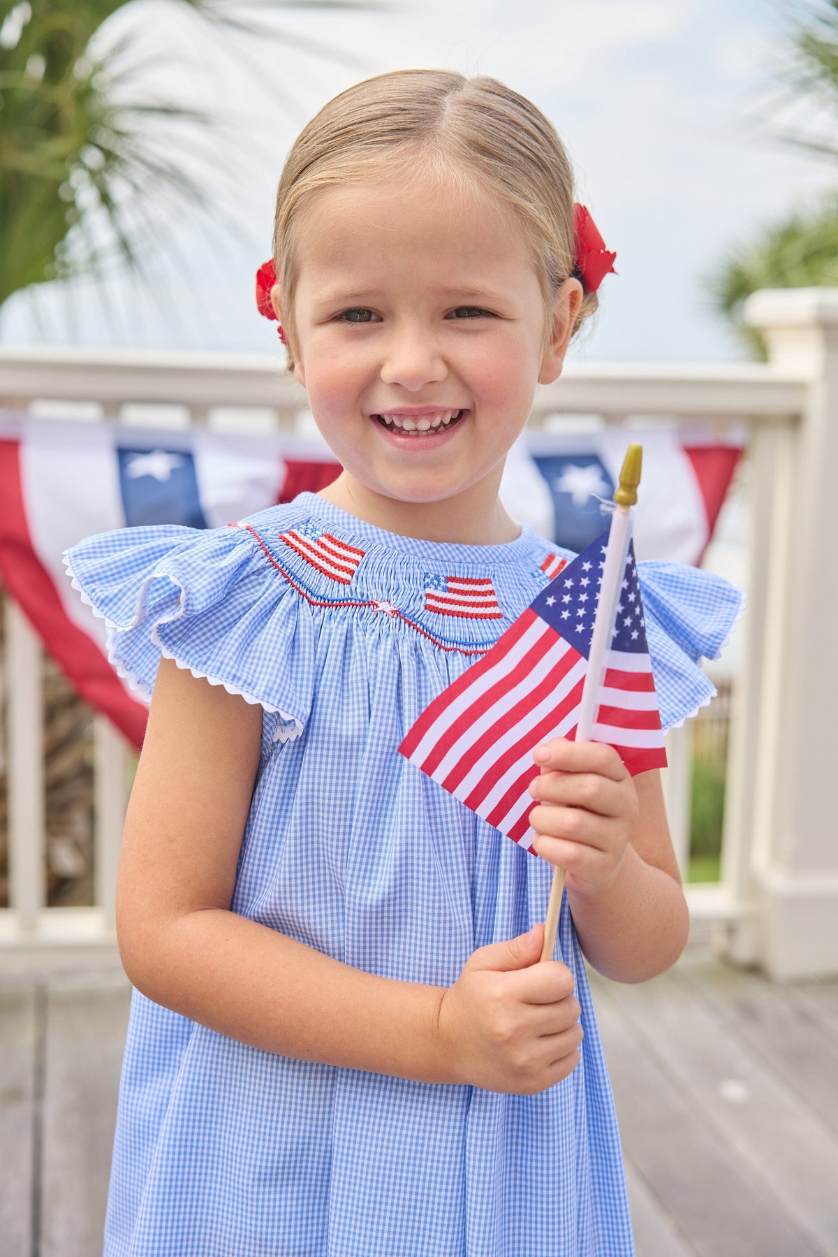 Little English traditional children's clothing. Flutter sleeve dress for toddler girls in royal blue mini gingham with smocking at the collar and American flag bunting