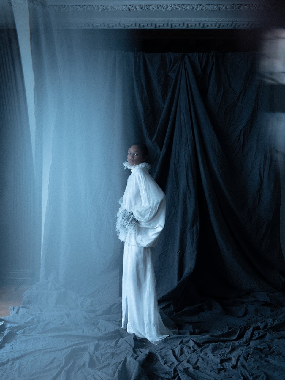 Full-length view of Anya Dress showcasing its flowing white fabric with blue and black draped curtains