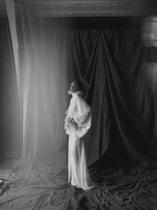 Side view of Anya Dress showcasing its floor-length flowing silhouette on a model against a draped backdrop