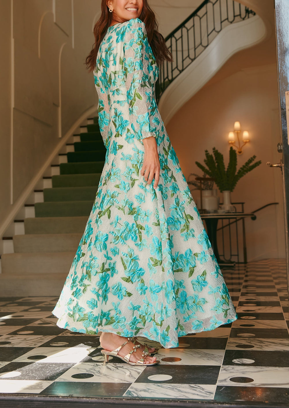Three-quarter back view of Brooke Gown in tropical turquoise organza showcasing sheer sleeves and a flowing floral skirt