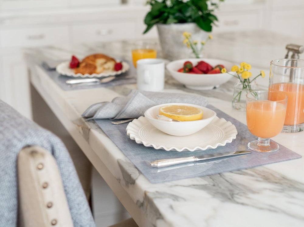 Stone chambray placemat under scalloped white plate and bowl with half lemon on marble counter, knife and juice glass