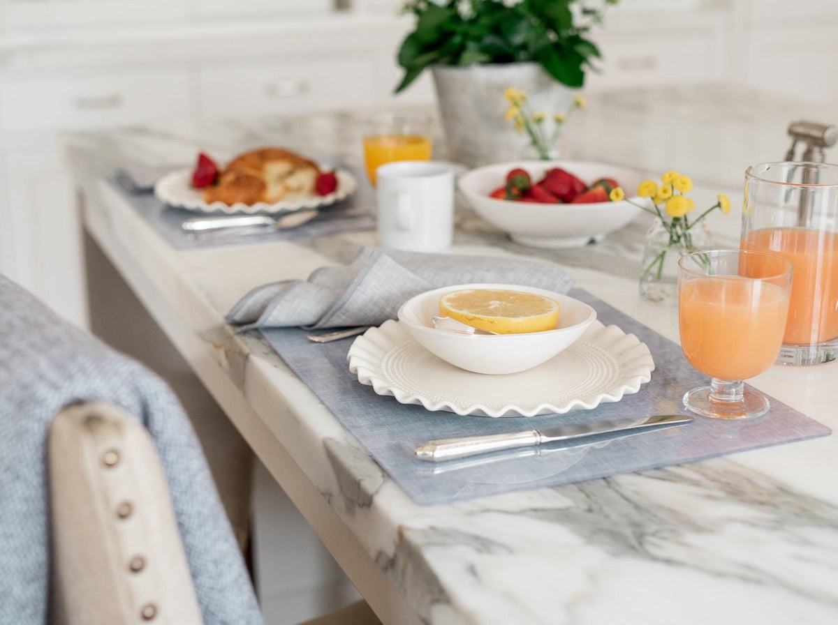 Stone chambray placemat under scalloped white plate and bowl with half lemon on marble counter, knife and juice glass
