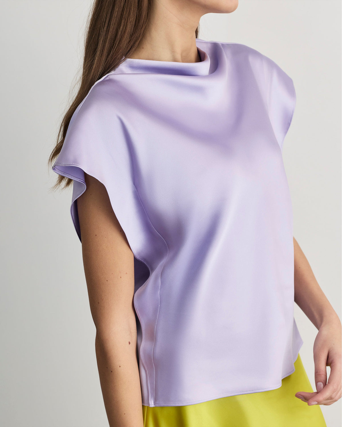 Side view of Adrien Top in lavender showcasing draped neckline and short flutter sleeves in satin crepe on a light neutral background