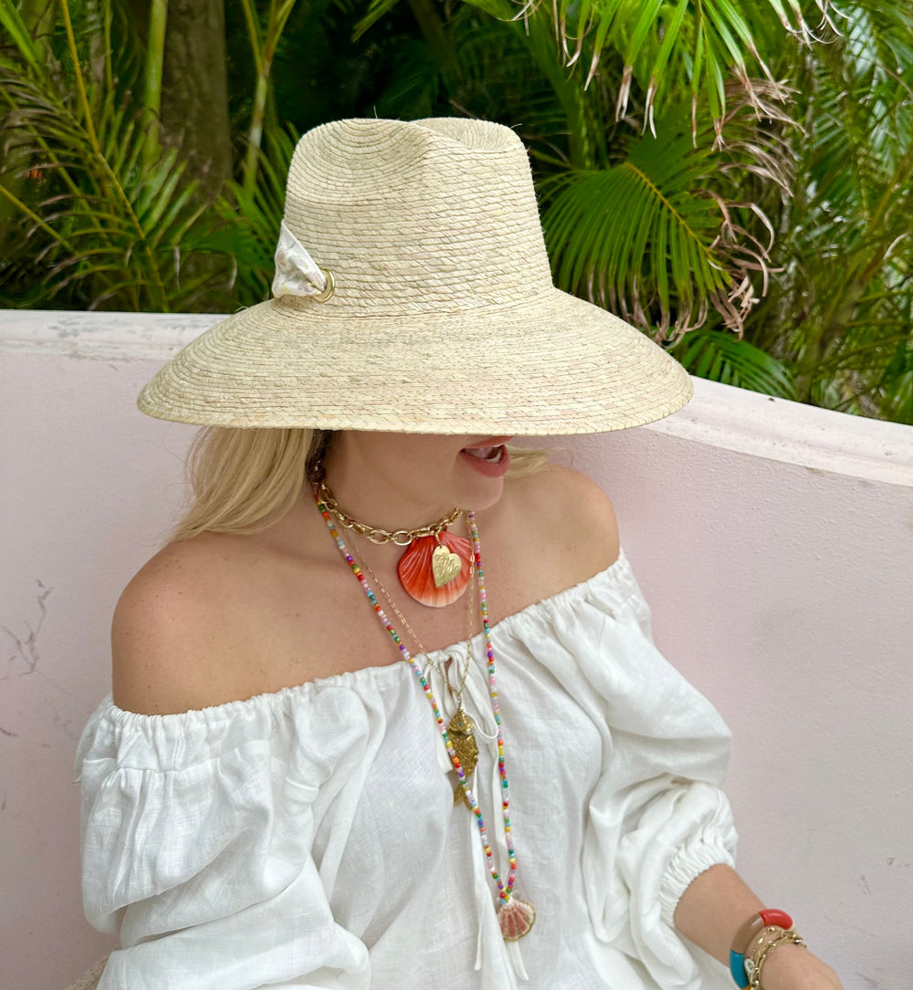 Side view of Hollyhock Sun Hat showing wide woven palm brim and navy grosgrain ribbon on model with pink wall background