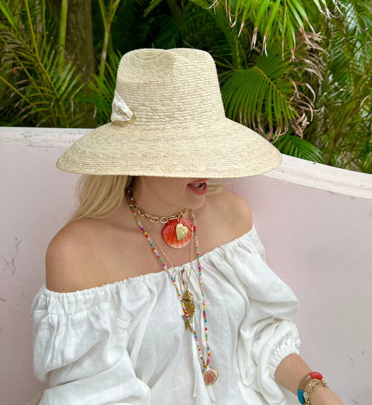 Side view of Hollyhock Sun Hat showing wide woven palm brim and navy grosgrain ribbon on model with pink wall background