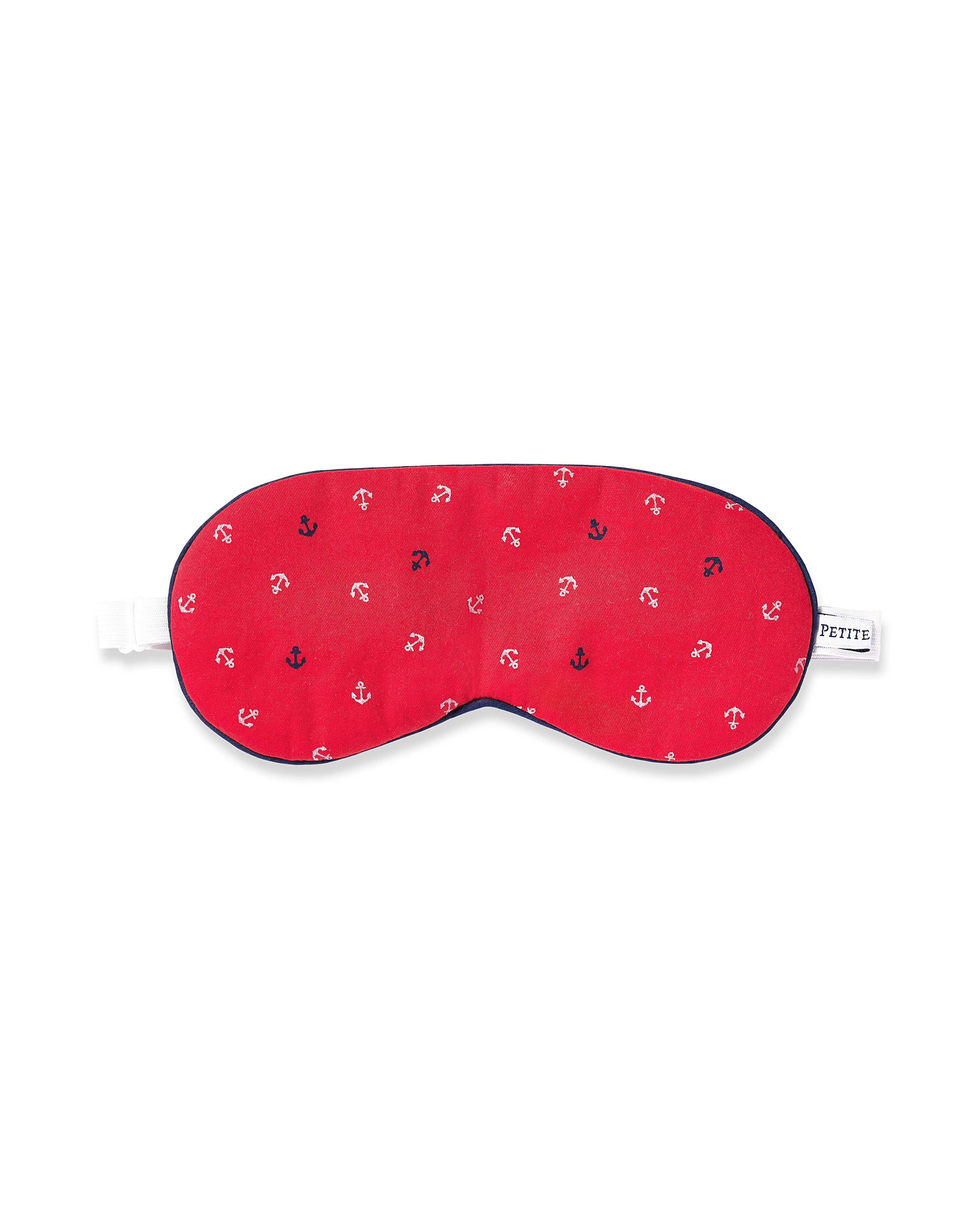 The Petite Plume Adults Twill Sleep Mask in Anchors Away features a red fabric with small white and navy anchors, a white elastic strap, and a side label, perfect for those seeking coordinated eye masks.