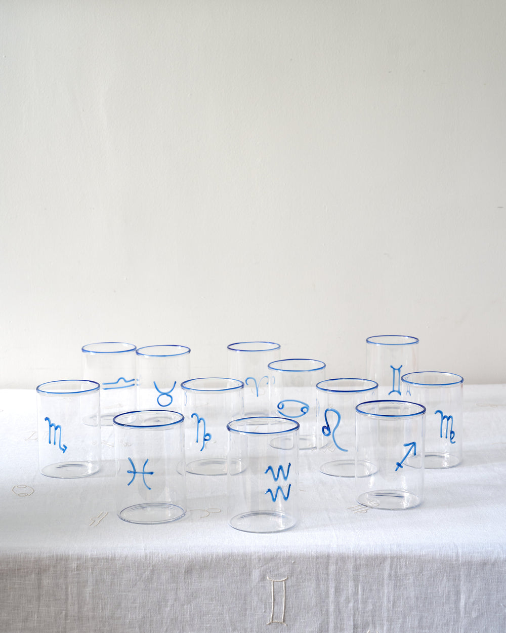 Front view of Aquarius lowball glass showcasing blue zodiac symbol and blue-rim detail on white linen background