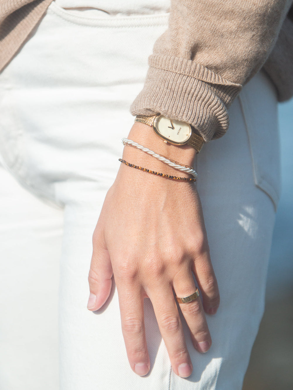 Model’s hand wearing the Alice bracelet in brown, tiger eye beads with freshwater pearl, layered with a gold watch and cream twisted bangle