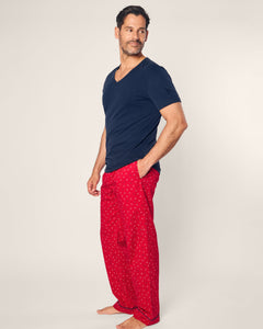 A man poses barefoot against a plain background, wearing a dark blue V-neck T-shirt and Petite Plumes Mens Twill Pajama Pant in Anchors Away, crafted from premium cotton with a small white print. With one hand in his pocket, he gazes thoughtfully to the side.