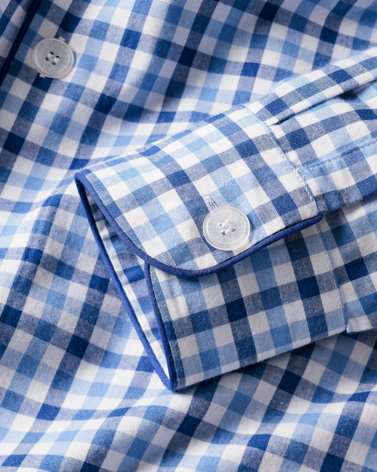 Close-up of the Mens Twill Pajama Set in Royal Blue Gingham by Petite Plume, highlighting a shirt cuff with a white button and alternating light and dark blue squares that embody the classic essence of gingham print.