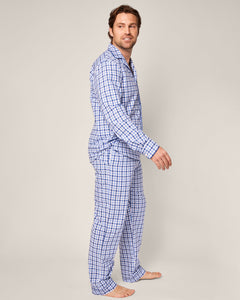 A person stands barefoot, turned slightly to the side, wearing the Mens Twill Pajama Set in Royal Blue Gingham by Petite Plume. They have short dark hair and smile against a neutral beige background.