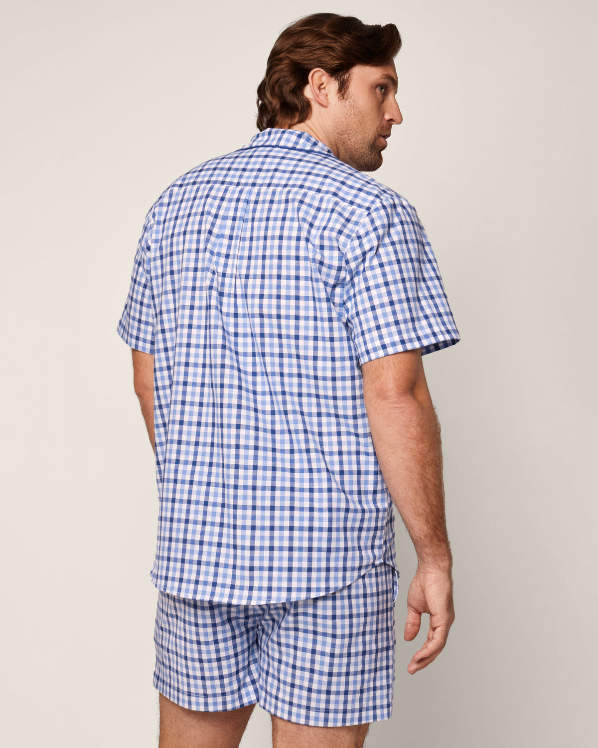 A man with brown hair is turned slightly to the side, wearing Petite Plumes Mens Twill Pajama Short Set in Royal Blue Gingham, expertly crafted from high-quality cotton, against a plain background.