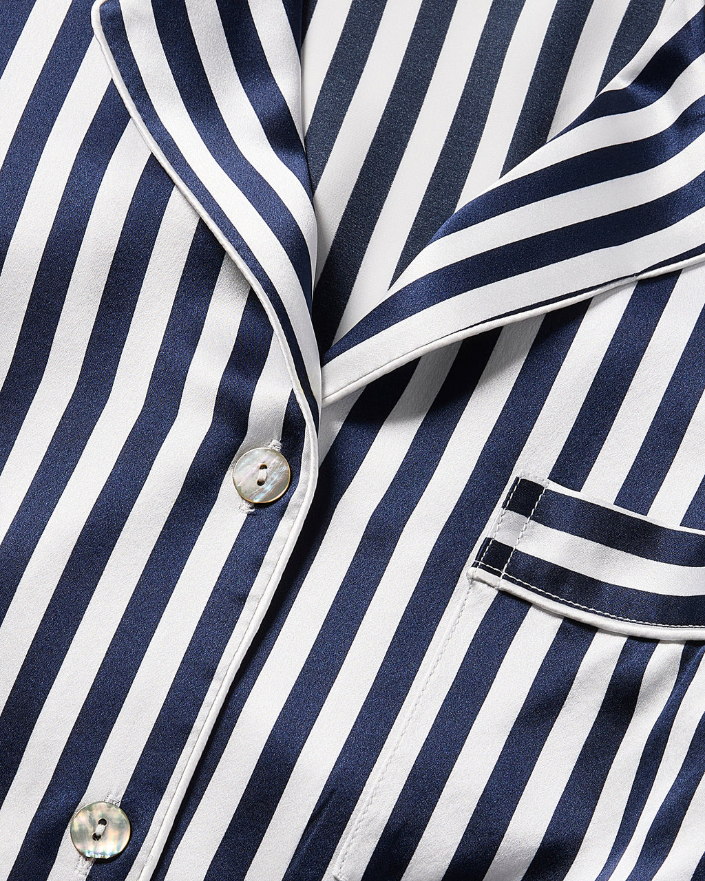 The Womens Silk Short Set by Petite Plume features a striped pajama top with navy Bengal and white vertical lines. It includes a collar, buttons, and a right-side pocket with matching trim, offering smooth, shiny luxury sleepwear in silk.