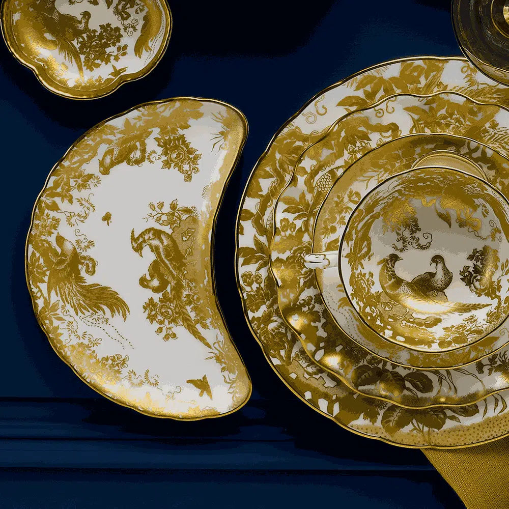 Top view of Aves dinnerware showing gold bird-and-floral pattern with 22 carat gold trim on white china on navy background