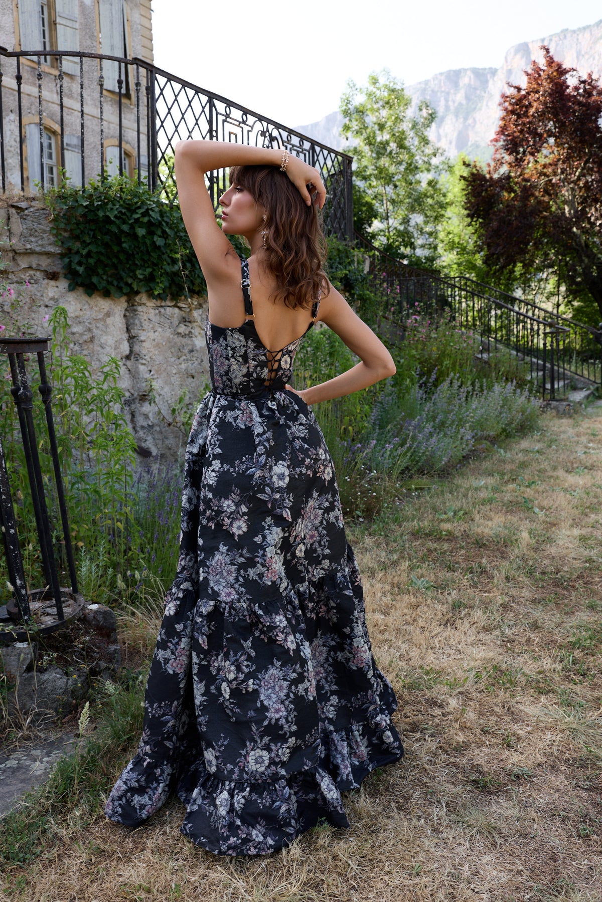 Back view of The Avery Dress in Black Lilibet Brocade showcasing multicolor floral brocade and gathered tiers in a garden