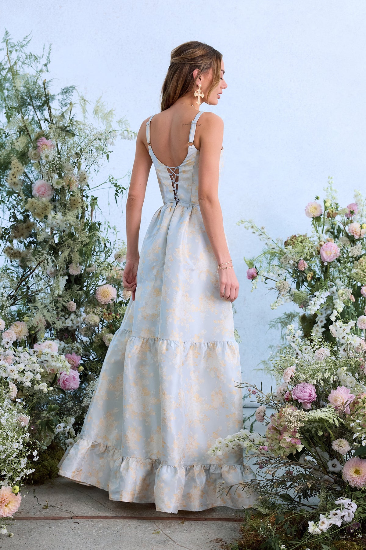 Rear view of The Avery Dress in Sky Windsor Brocade showcasing lace-up corset and tiered skirt with floral backdrop