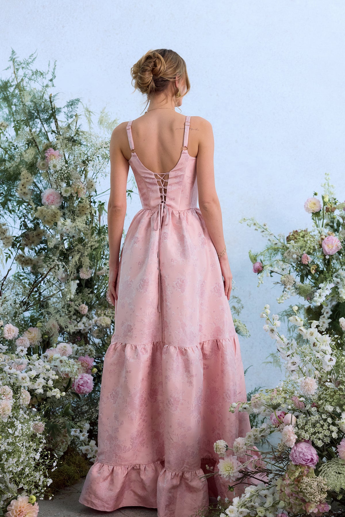 Back view of The Avery dress in light pink Windsor brocade with lace-up back, adjustable straps and tiered ruffle skirt