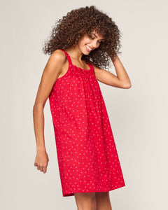 A woman with curly hair beams in a Petite Plume sleeveless red dress, the Womens Twill Annabelle Nightgown in Anchors Away, adorned with delicate nautical patterns of small white flowers, standing against a plain background.