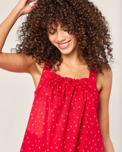 A person with curly hair smiles while touching their head, wearing the Petite Plume Womens Twill Annabelle Nightgown in Anchors Away. The red dress features small nautical white patterns, and the plain light-colored background adds charm to the scene.