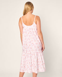 A person with long blonde hair is wearing the sleeveless Womens Twill Chloe Nightgown in Seashell Splendor by Petite Plume. Crafted from soft cotton, it features a pink floral design and a loose fit, reaching below the knees as the person faces away from the camera against a plain background.