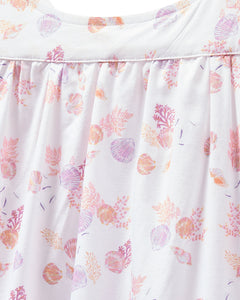 Close-up of Petite Plumes Womens Twill Chloe Nightgown in Seashell Splendor, featuring a white cotton fabric with pink and purple seashells and coral patterns. The luxury sleepwear displays gentle folds and has a soft texture.