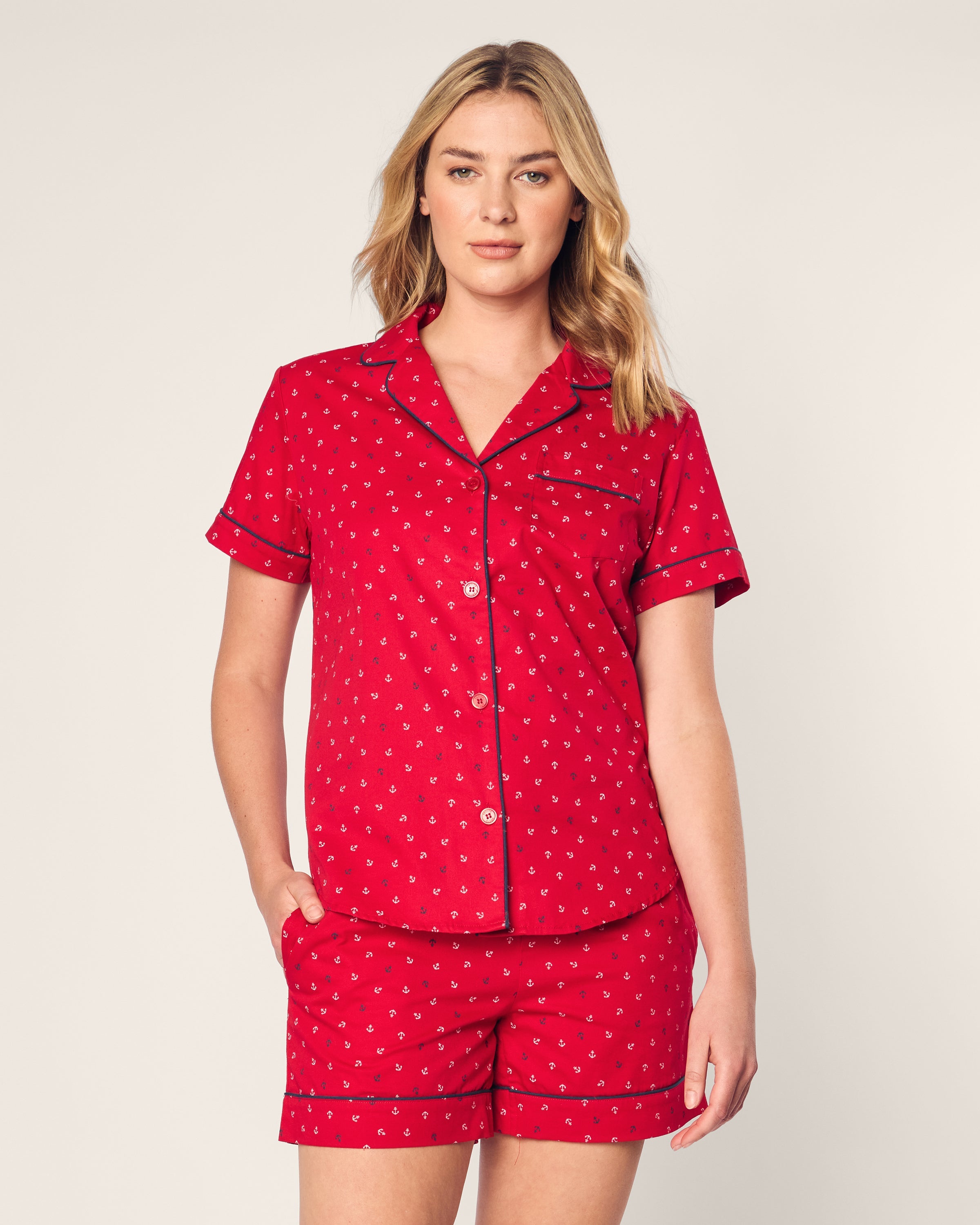 A person models the Petite Plume Womens Twill Short Sleeve Short Set in vibrant red with an Anchors Away print, featuring a collared button-down shirt and shorts against a plain, light background.
