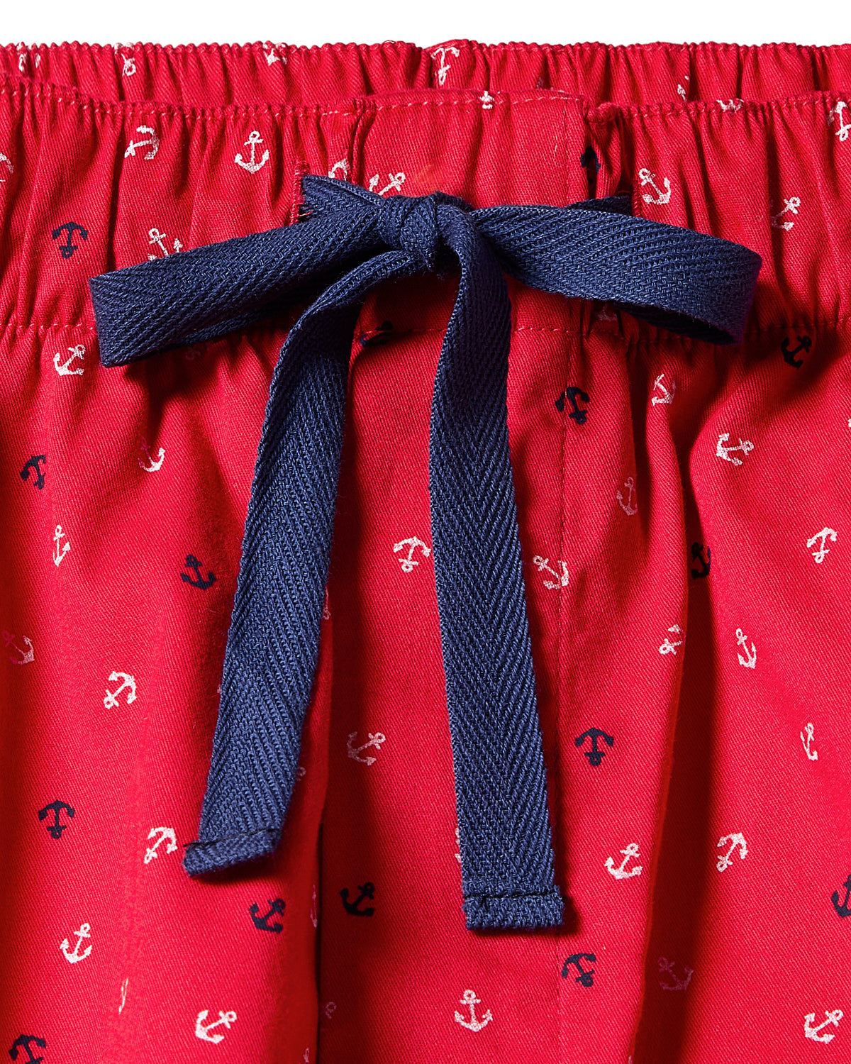 The Womens Twill Short Sleeve Short Set in Anchors Away by Petite Plume is a luxurious cotton sleepwear set featuring red fabric, blue drawstring, and an Anchors Away pattern of small white and navy anchors, finished with a bow at the center.