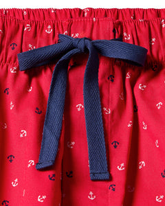 The Womens Twill Short Sleeve Short Set in Anchors Away by Petite Plume is a luxurious cotton sleepwear set featuring red fabric, blue drawstring, and an Anchors Away pattern of small white and navy anchors, finished with a bow at the center.