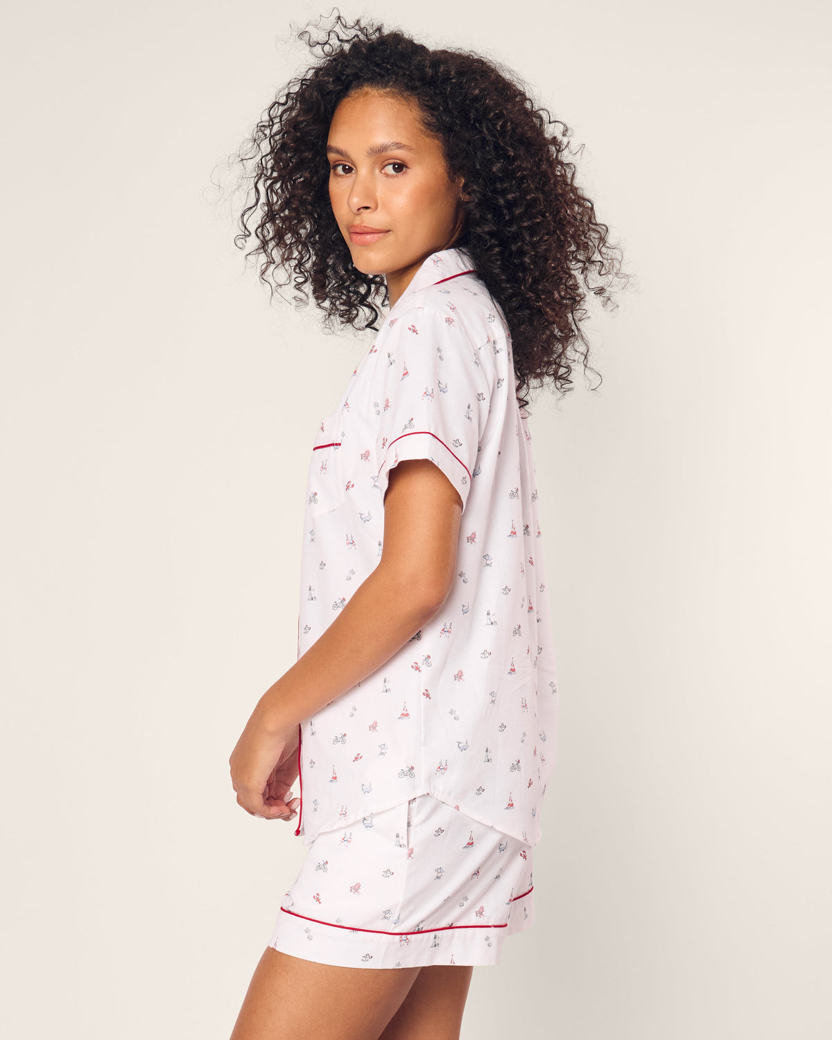 A person with curly hair wears the Womens Twill Short Sleeve Short Set in Coastal Charms by Petite Plume, featuring a subtle pattern. They stand gracefully, looking over their shoulder against a plain background.