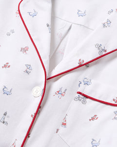 Close-up of Petite Plumes Womens Twill Short Sleeve Short Set in Coastal Charms, featuring a white pajama shirt with red piping and whimsical prints of whales, lobsters, bicycles, and beach umbrellas. Made from premium cotton, it includes a button closure and a pocket with matching trim.