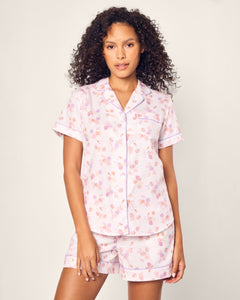 A person with curly hair wears Petite Plumes Womens Twill Short Sleeve Short Set in Seashell Splendor, crafted from luxurious cotton. The light-colored floral pajama set features a short-sleeved collared top and matching shorts against a plain background.