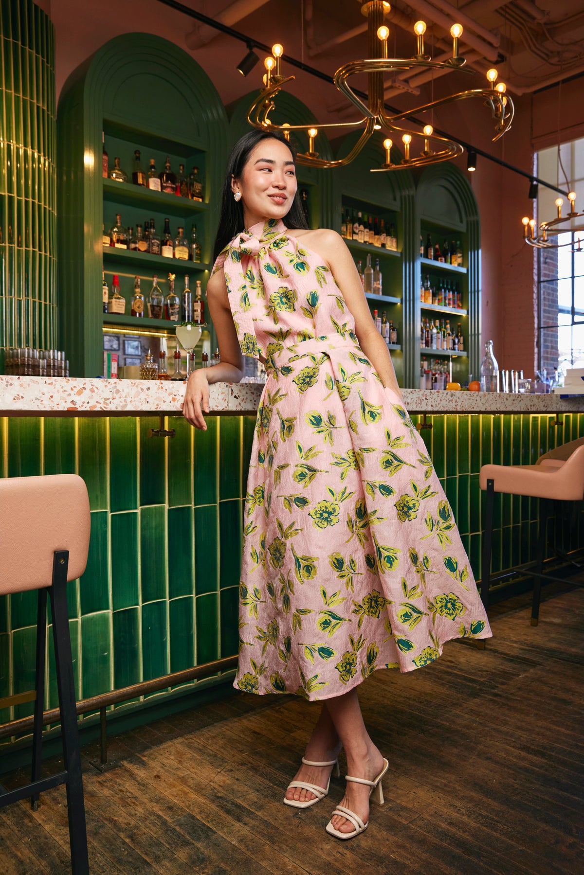 Model wearing the pink Eden midi skirt with bright floral jacquard in a warmly lit bar