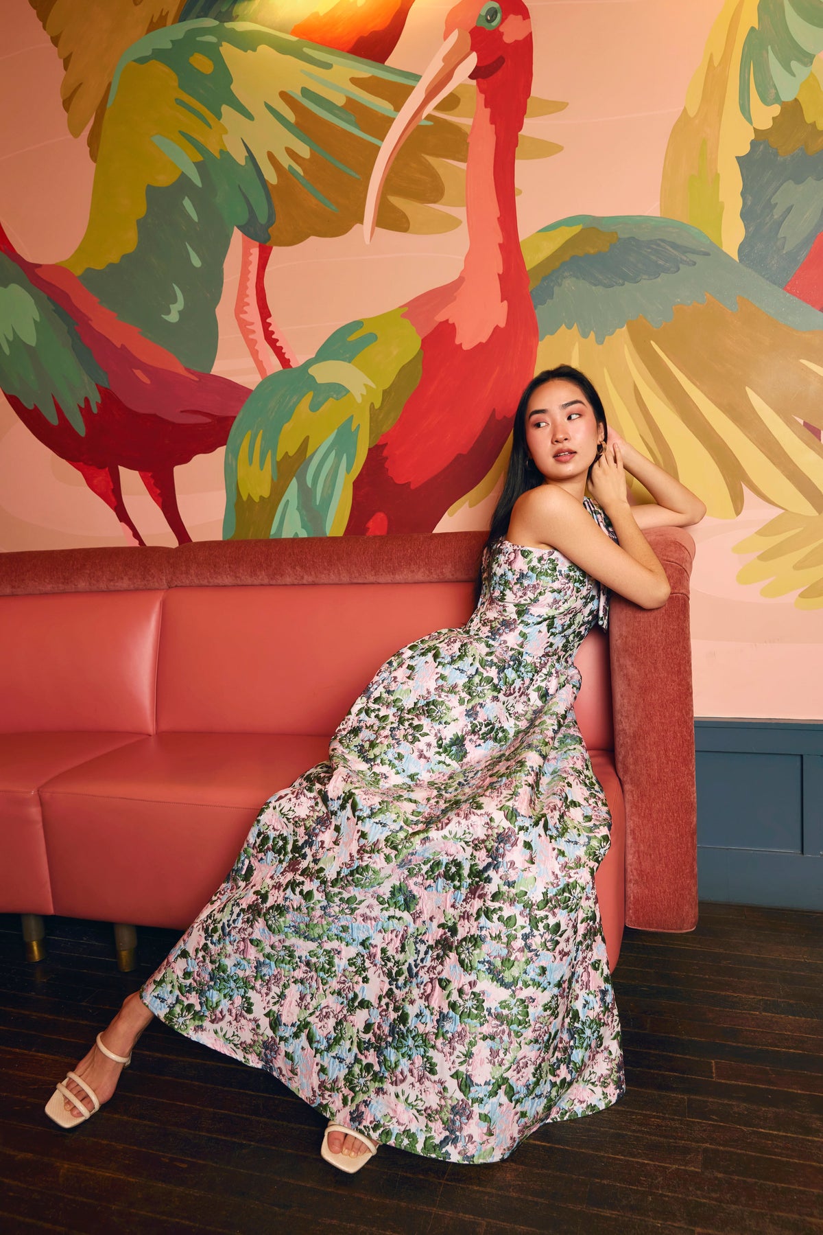 Three-quarter view of Caroline gown in pink floral jacquard showcasing one-shoulder bow and full A-line skirt against mural