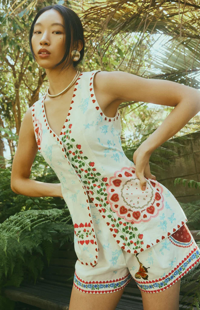 Three-quarter front view of Alexa Top in Alfie White showing V-neck sleeveless fit with red heart and floral print in a garden setting