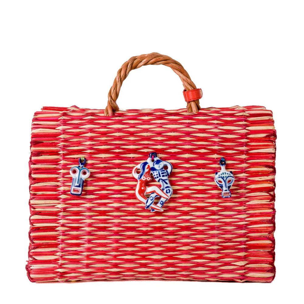 Front view of Amor large basket bag showing red-and-natural woven reeds, three porcelain charms, braided leather handle on white