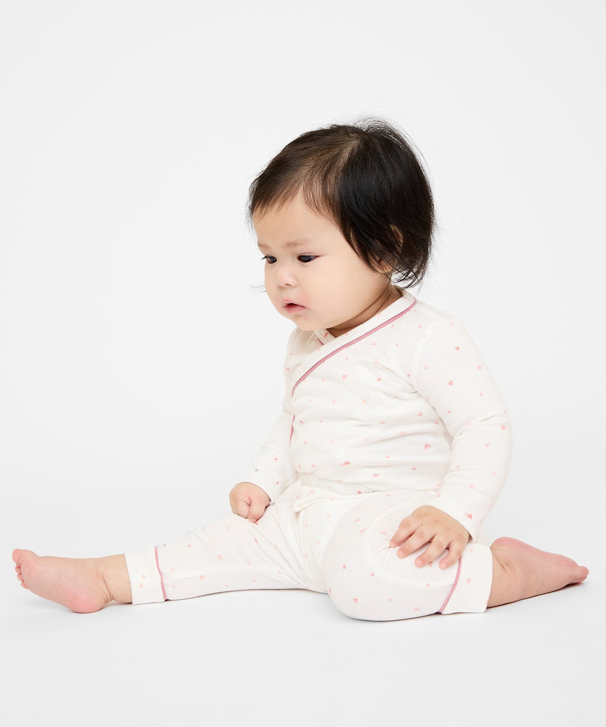 Seated baby wearing Andy Baby Legging in Rose Hearts with cuffed hems, pink contrast piping and small heart print on white background