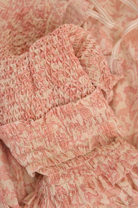 The Anita Dress has a diamond-smocked bodice, flutter cap sleeves, a back tie, and a bubble skirt.