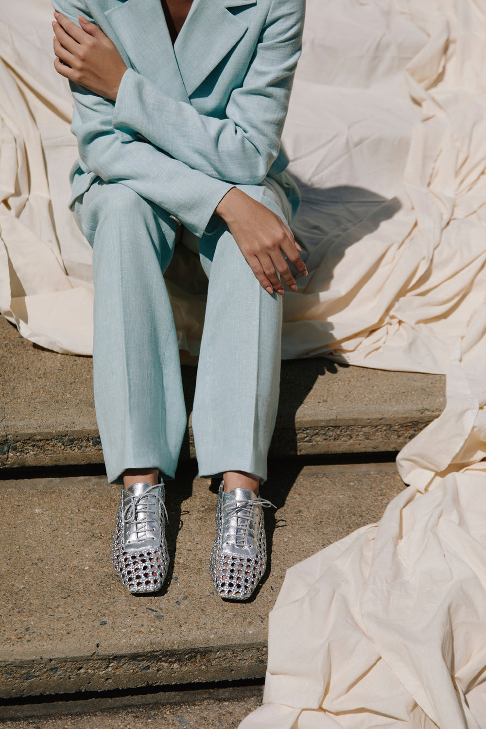 Front view of Antonia flat leather oxford in silver showing woven cutout upper and lace-up detail on concrete steps