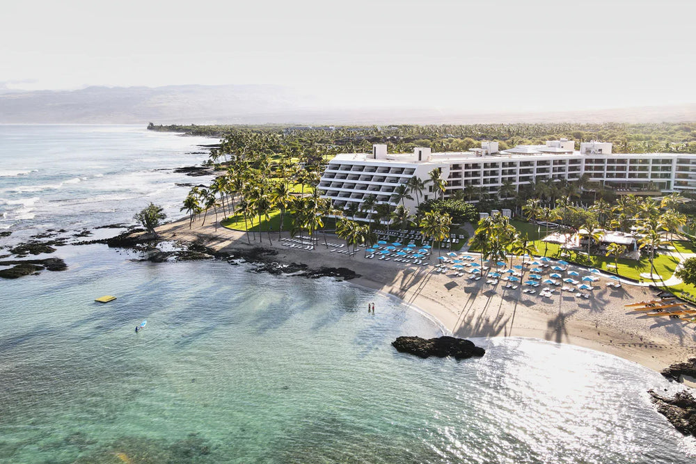 Aerial view of Mauna Lani resort on a palm-lined beach with lounge chairs and calm turquoise ocean