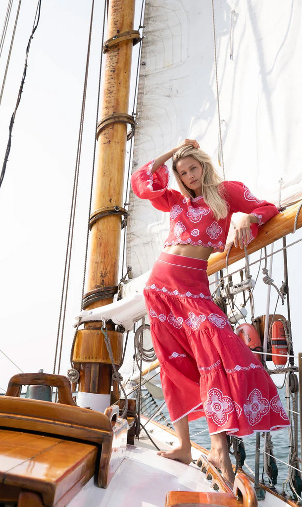 Model wearing Scarlet Willow tiered red linen skirt with clover embroidery, scalloped hem, and tiered silhouette on sailboat