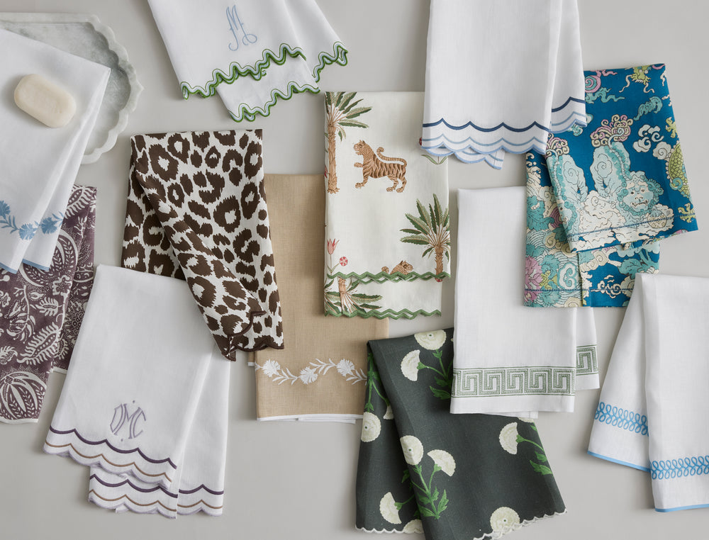 Overhead flat lay of Ophelia guest towels showcasing embroidered Greek-key tape and scalloped hems in assorted colors and prints on a light gray background
