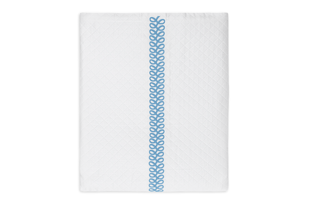 Top-down view of Astor Braid Matelassé coverlet with central blue braid embroidery and diamond-quilted pattern on white