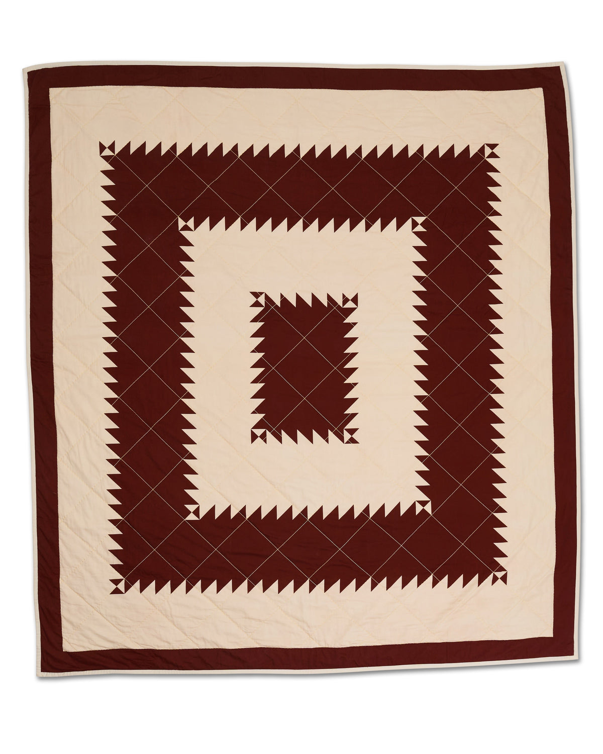 Flat lay of Maurier quilt showcasing burgundy sawtooth concentric squares on cream cotton with diamond stitching